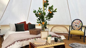A cozy tented accommodation with a bed, a wicker side table, and a chair with a patterned cushion. - Countryside Avon Escape for Two (Pewsey)