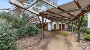 A covered outdoor area with a dirt path leading to a building with a wooden bench. - Old Lonnie Crigan RD (Point Lonsdale)