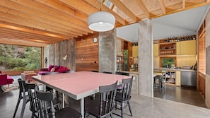 A modern kitchen with wooden cabinetry, a dining area with a pink table, and a view of the outdoors. - Old Lonnie Crigan RD (Point Lonsdale)