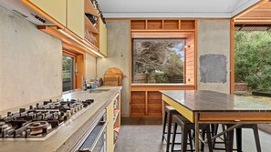 A modern kitchen with a gas stove, wooden cabinets, and a large window overlooking a garden. - Old Lonnie Crigan RD (Point Lonsdale)