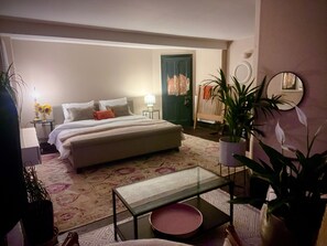 Ein Schlafzimmer mit einem Bett, Nachttischen, einem Glastisch, einem Sessel und Topfpflanzen.