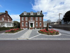 En toetages murstensbygning med en grøn dør, en grusbelagt indkørsel og røde blomster i forgrunden.