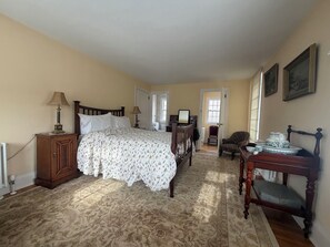 A bedroom with a bed, a wooden nightstand, a desk, a chair, and a radiator.