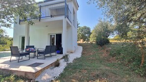 Ein modernes, zweistöckiges Gebäude mit Balkon, Sitzgelegenheit im Freien und einem Pool.