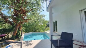 Ein Swimmingpool mit Liege und Tisch, umgeben von Bäumen und einem Gebäude.