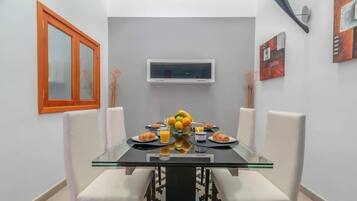 A dining area with a glass table, white chairs, and a fruit bowl.