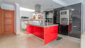 Une cuisine moderne avec un îlot central rouge, des appareils électroménagers intégrés et une porte en bois.