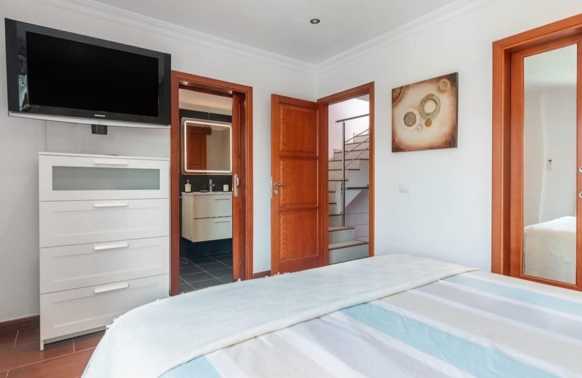 A bedroom with a bed, a TV, a wardrobe, a bathroom, and a staircase.