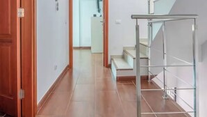 Un couloir doté d’un plancher en bois, d’une porte en verre et d’un escalier avec des rampes en métal.