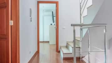 A hallway with a wooden floor, a glass door, and a staircase with metal railings.