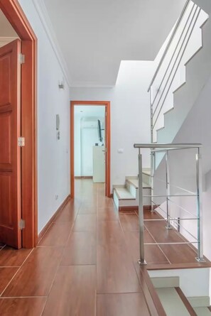 Ein Flur mit Holzboden, Glastür und einer Treppe mit Metallgeländern.