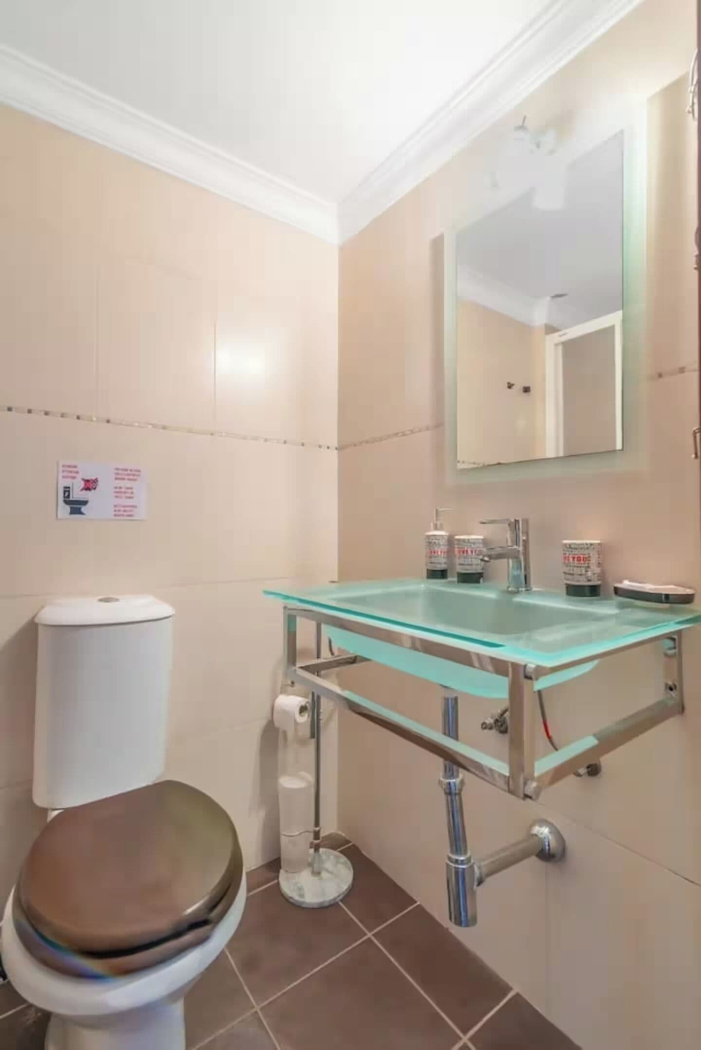 A bathroom with a glass sink, a toilet, and a mirror.