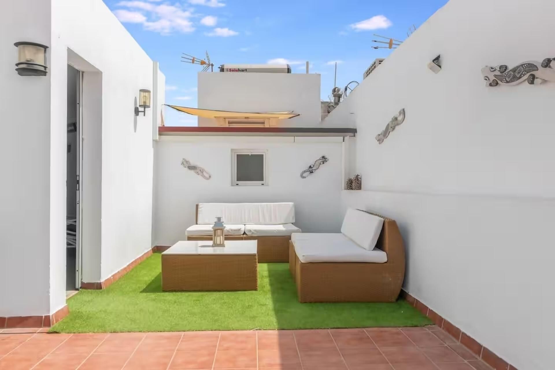 A small, enclosed outdoor living space with a sofa and a table, a door leading to a covered area, and a small window.