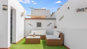Un petit espace de vie extérieur, à l’abri, comprenant un canapé et une table, une porte donnant sur une zone couverte et une petite fenêtre.