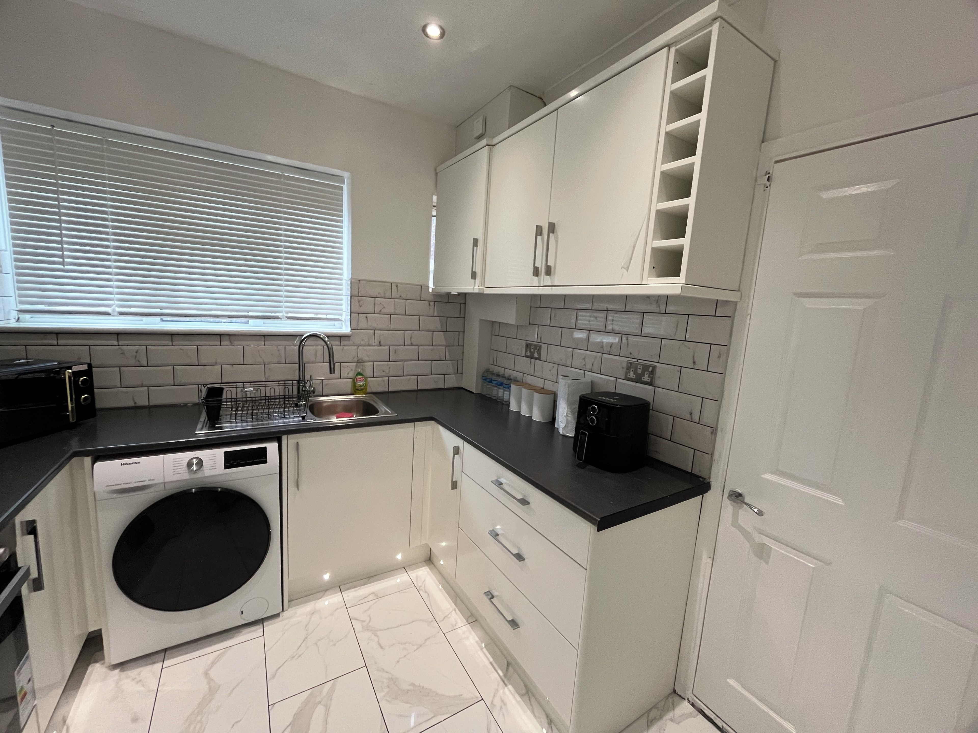 A compact kitchen with a built-in washing machine, a sink, and a window with blinds.