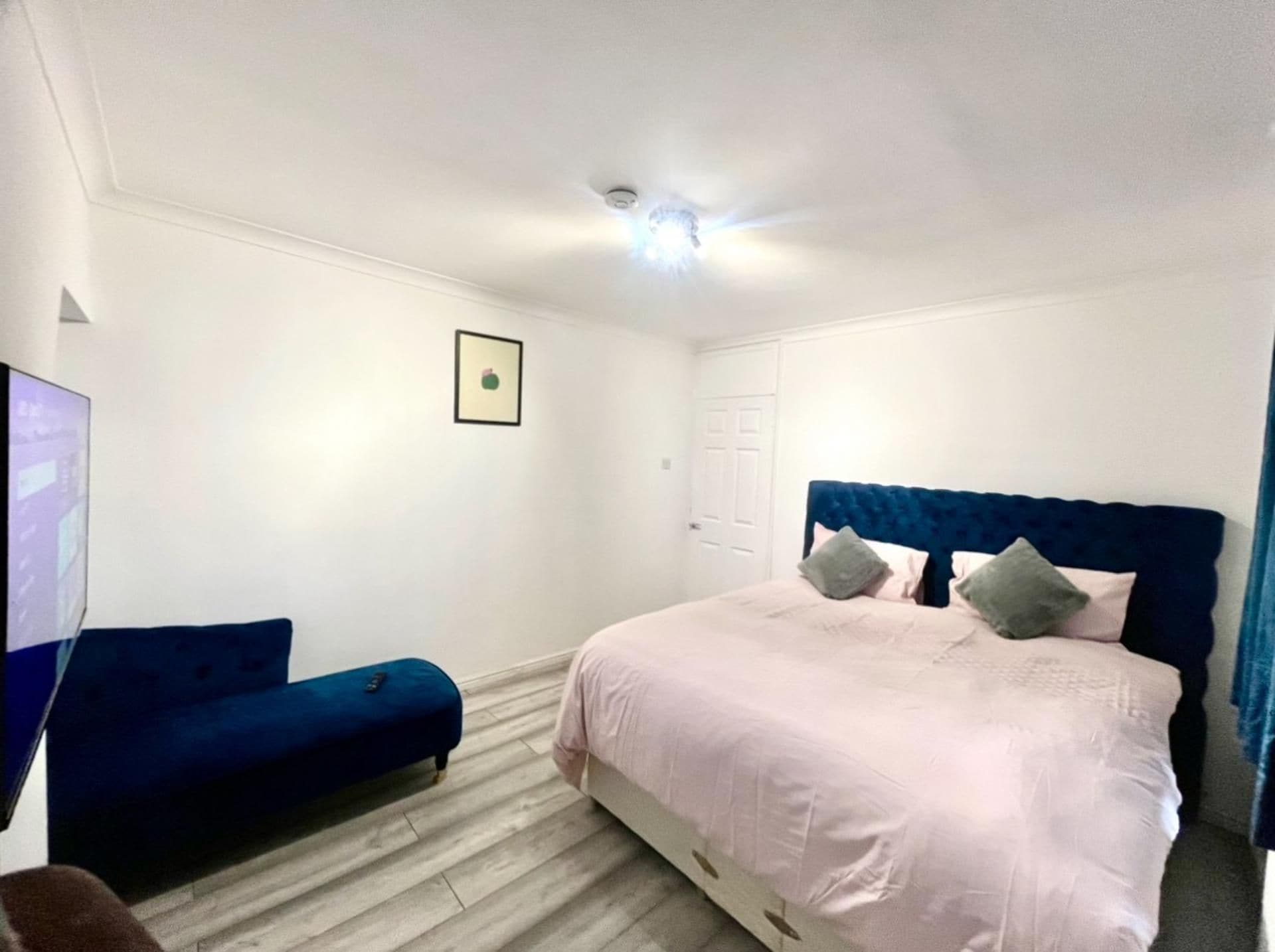 A bedroom with a bed, a blue sofa, a white door, and a ceiling light.