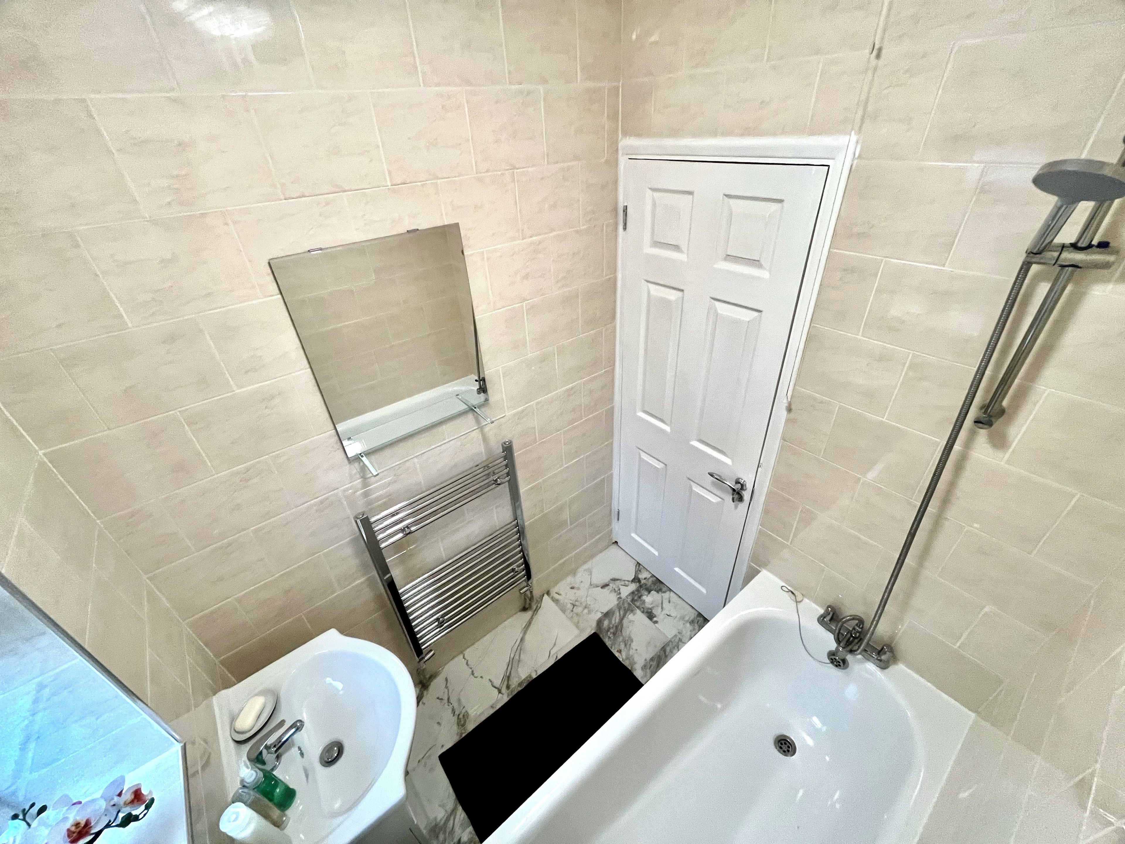 A bathroom with a white bathtub, a sink, a mirror, and a door.