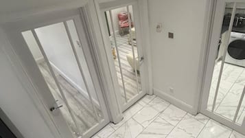 Una habitación con un amplio ventanal corredizo que da a un balcón, suelo de baldosas blancas y un banco acolchado marrón.
