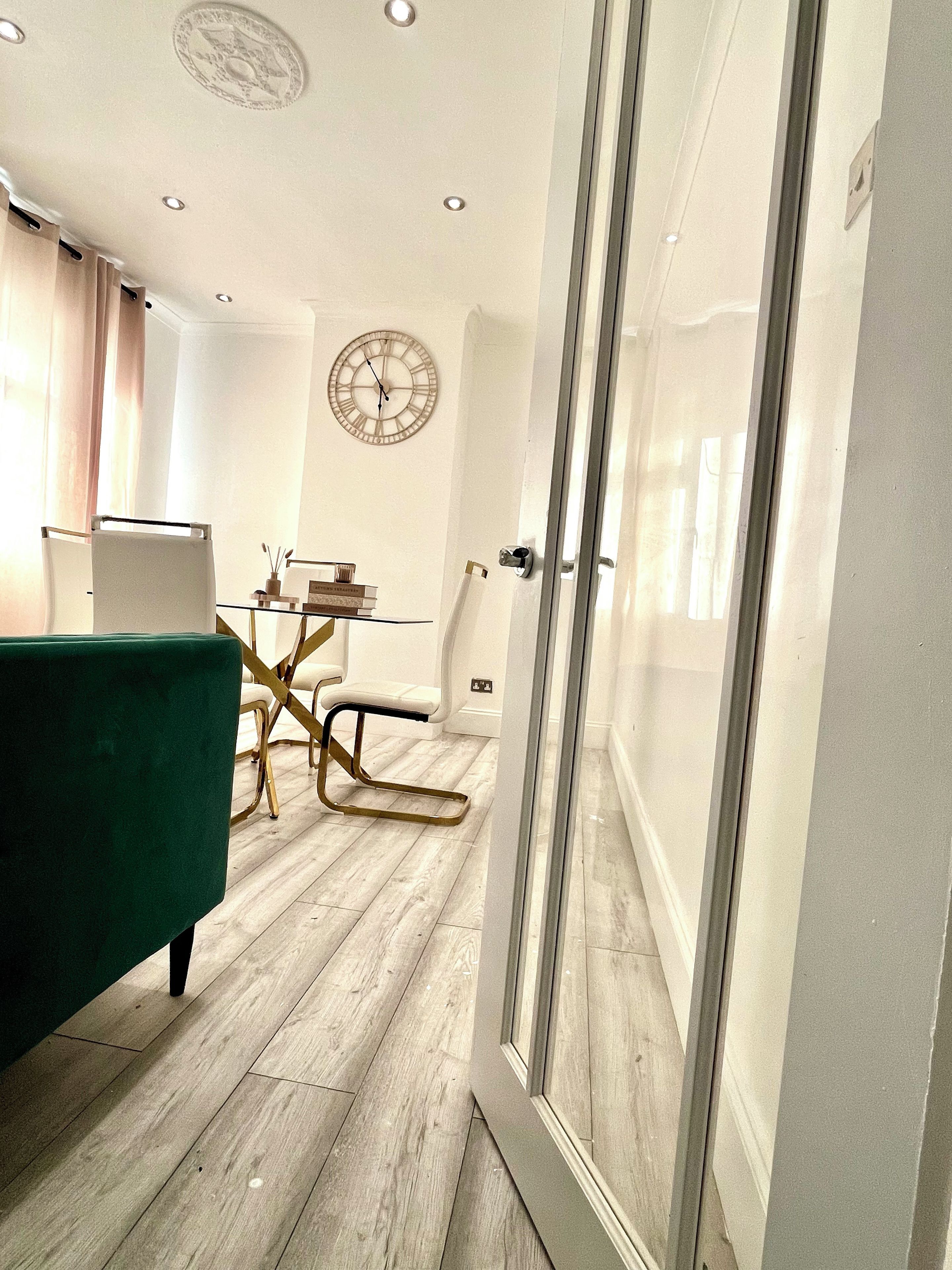 Un interior moderno con una zona de comedor, una silla tapizada en verde, piso de madera y un reloj de pared.