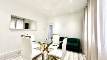 A modern dining area with a glass table, white chairs, and a green sofa.
