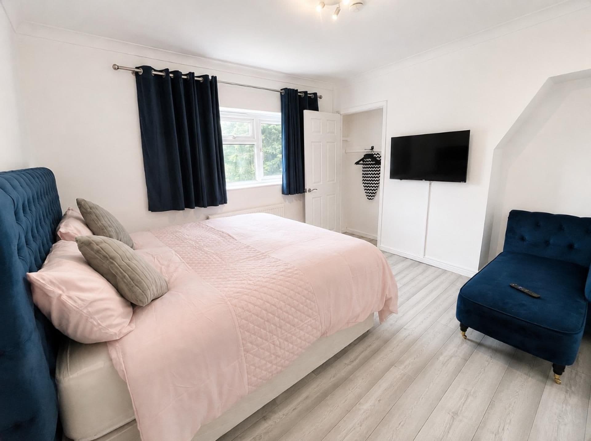 A bedroom with a bed, a TV, a chair, and a window with curtains.