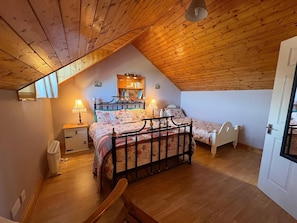 A cozy attic bedroom with a sloped ceiling, two beds, a nightstand, a lamp, and a bookshelf.