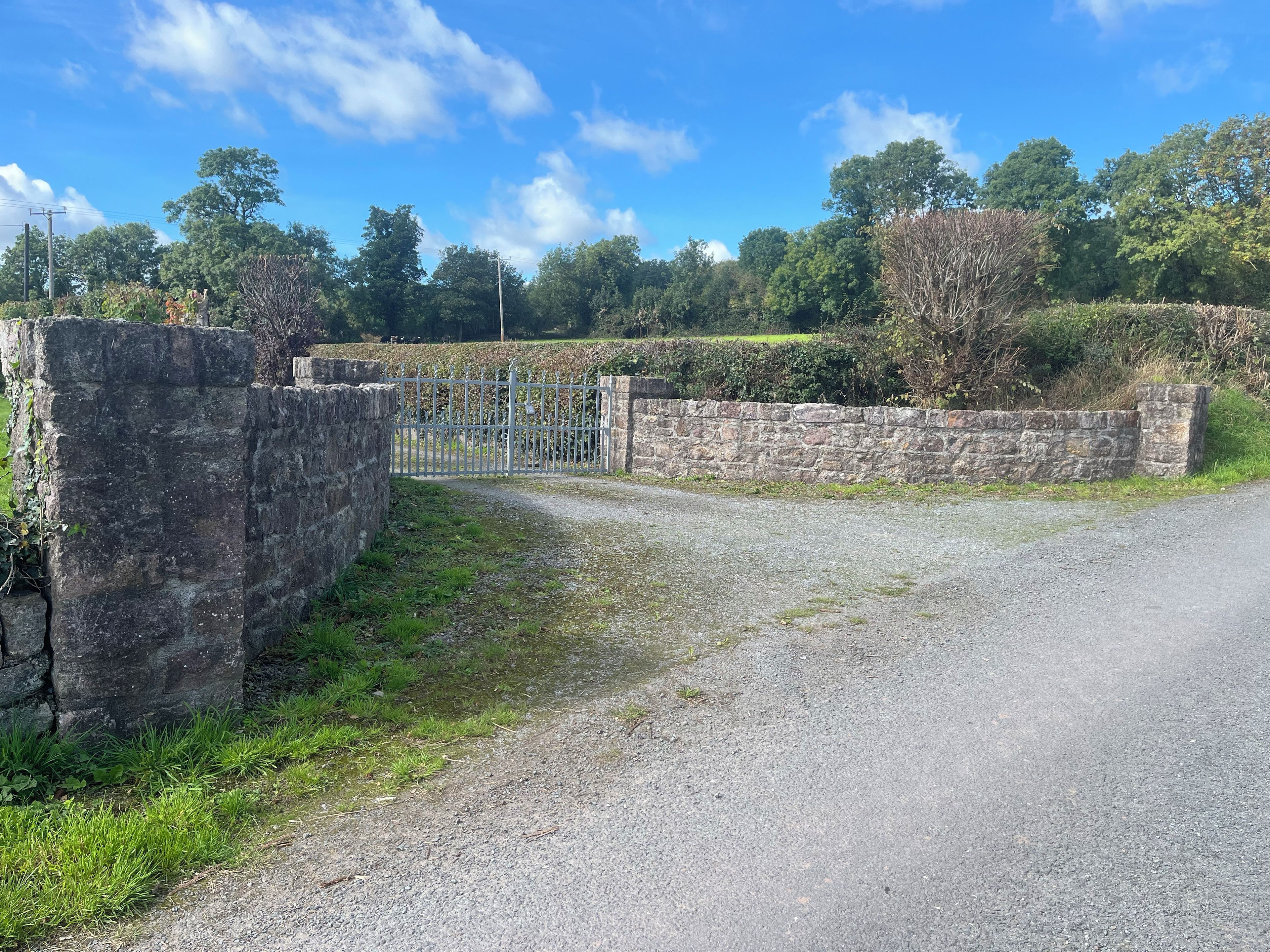 A rural road leading to a gated area with stone walls and a metal gate.