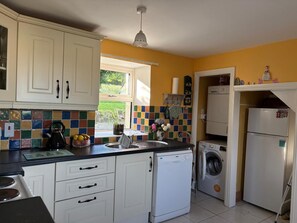 A compact kitchen with white cabinets, a tiled backsplash, a washing machine, and a refrigerator.