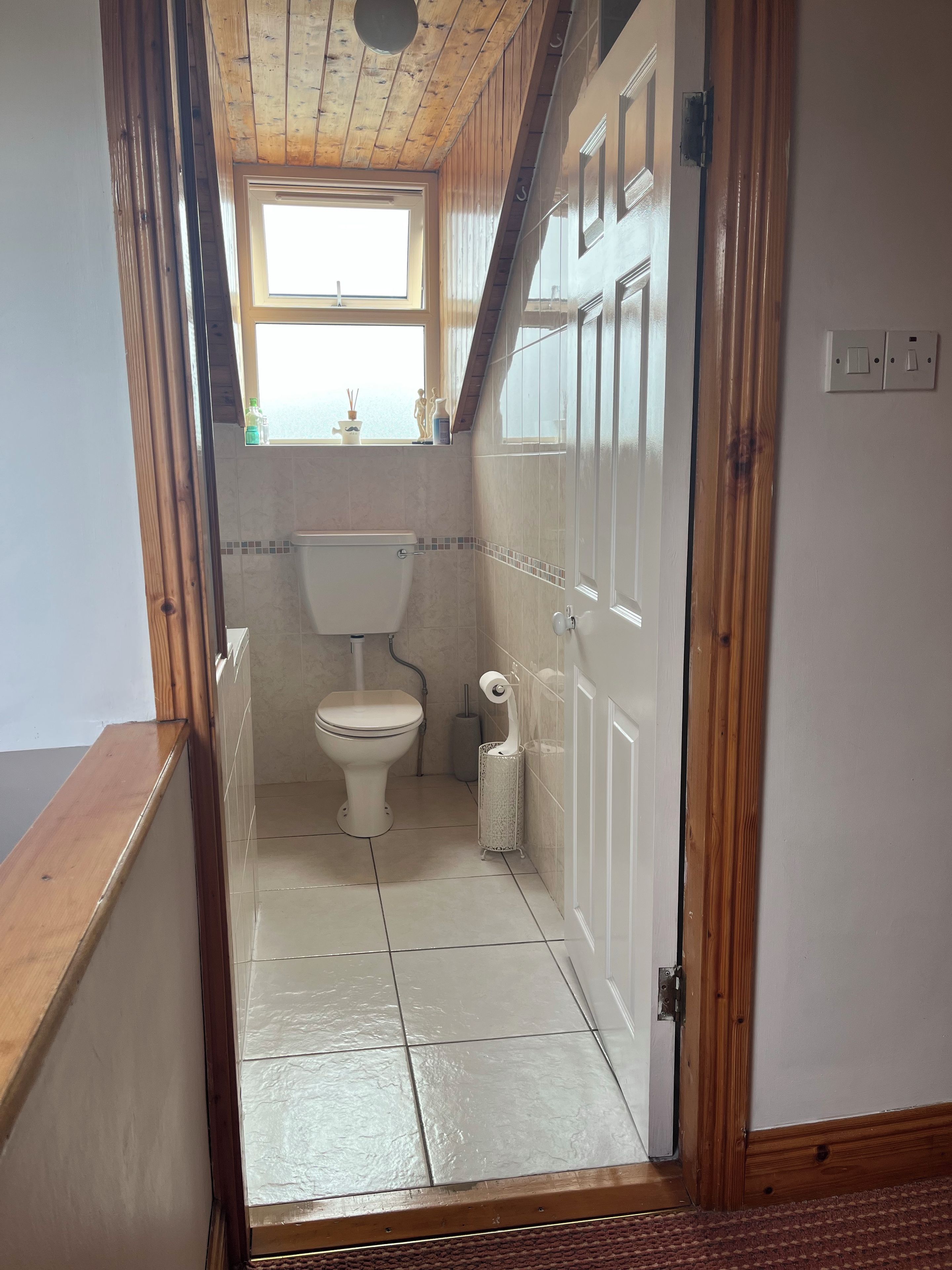 Ein schmales Badezimmer mit Toilette, einem Fenster und Fliesenboden.