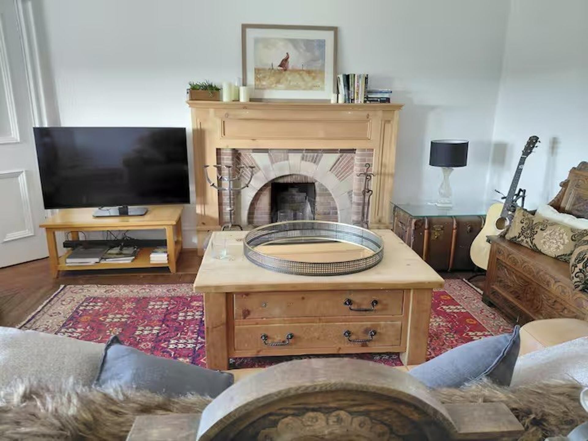 A living room with a fireplace, a television, a guitar, and a sofa.