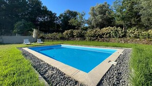 Una piscina rectangular con superficie de agua azul cristalina, rodeada por un borde de piedra y una zona verde.