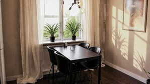 A dining area with a table and chairs, a window with curtains, and a hanging light fixture.