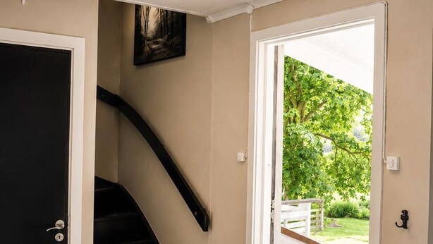 A modern interior with a staircase, a door leading outside, and a black mat at the entrance.