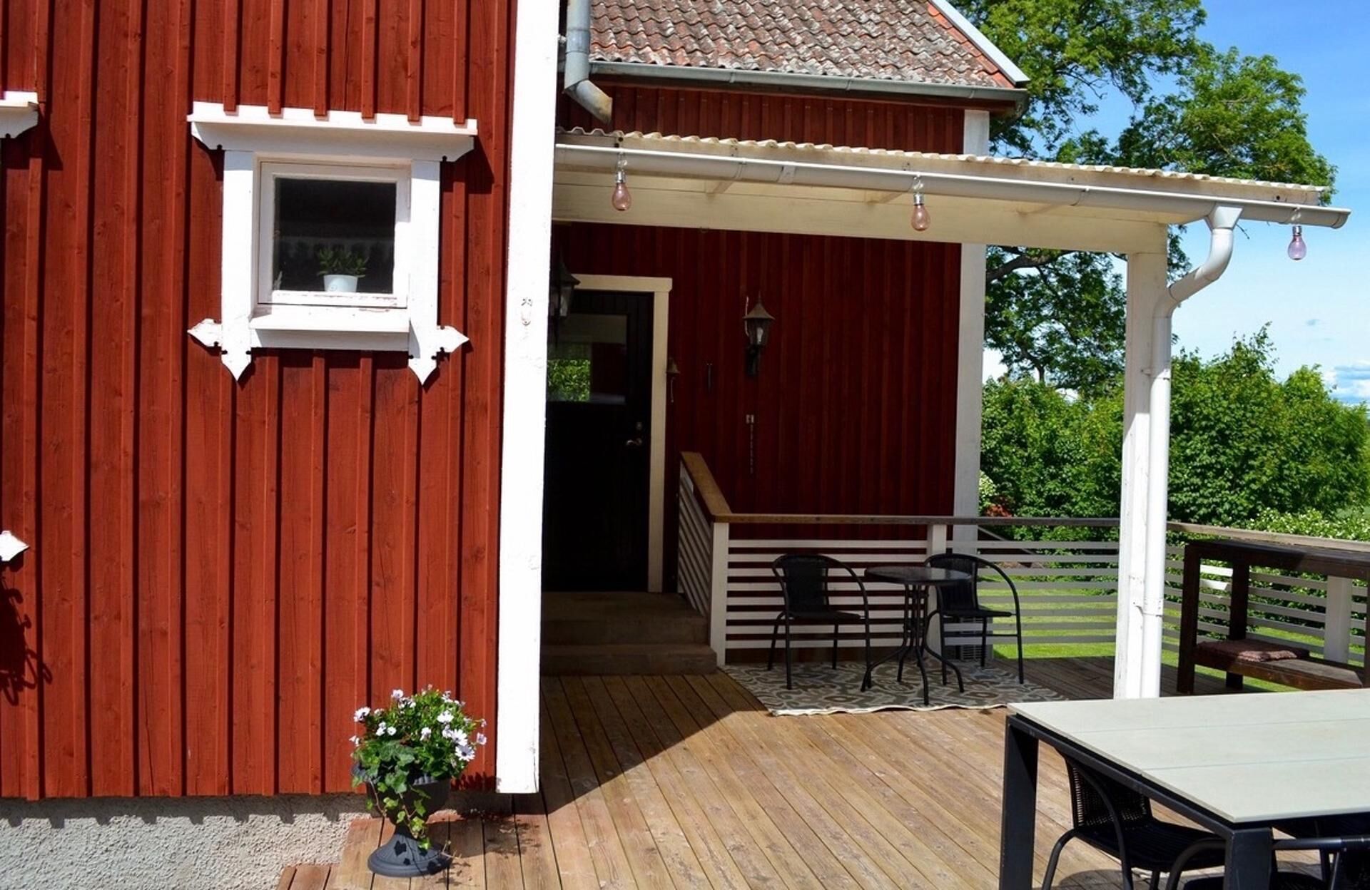 Punainen rakennus, jossa on katettu kuisti, pieni ikkuna ja ruukussa oleva kasvi.