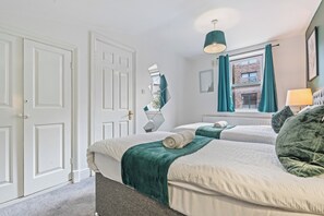 A bedroom with two beds, a window with curtains, a mirror, and a lamp.