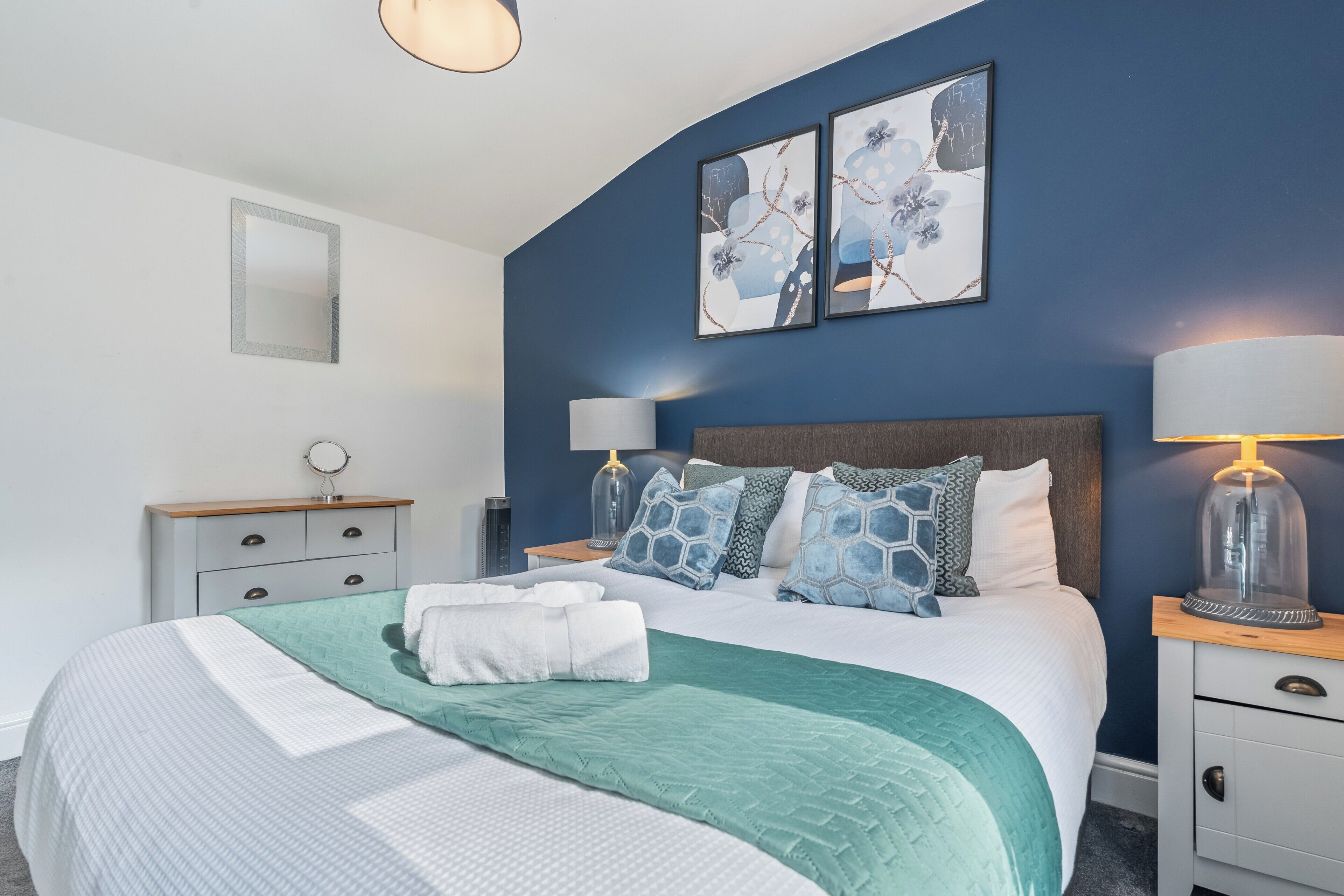 A bedroom with a bed, two bedside tables, a mirror, and artwork on the wall.