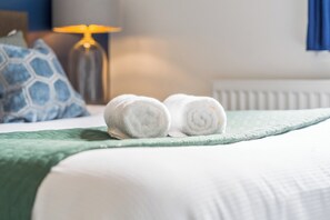 A neatly made bed with a green bedspread and two rolled white towels placed on it.