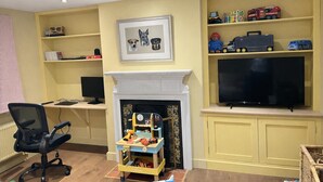A living room with a fireplace, a television, and shelves with toys and books. - Riverside Cottage Sleeps 8 With Parking (Marlborough)