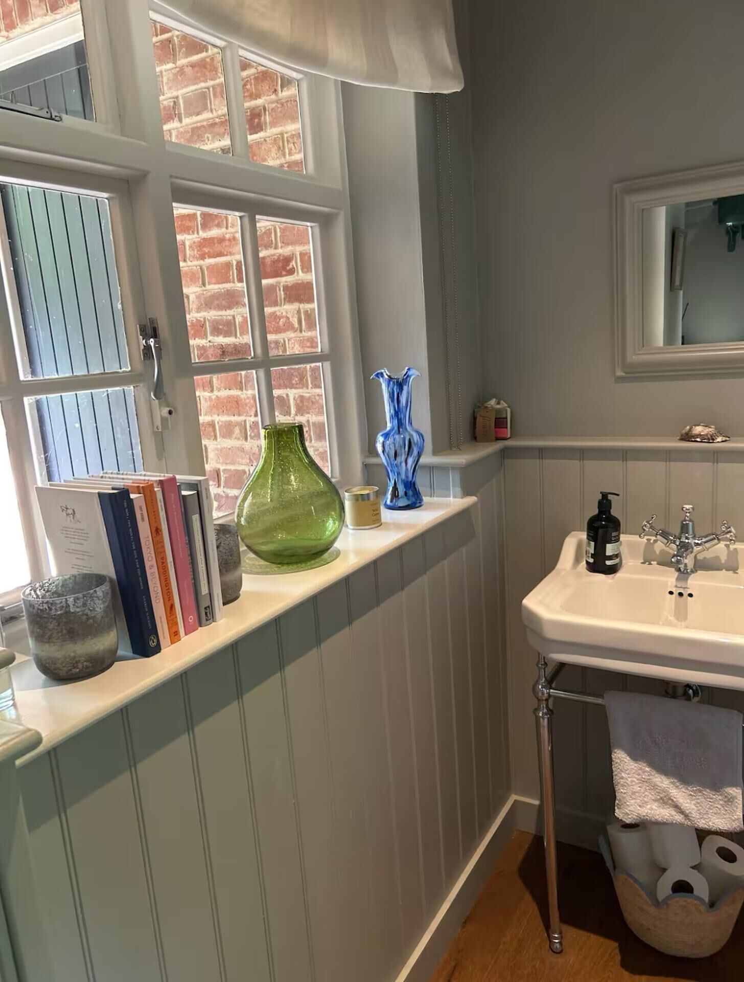 A bathroom with a white sink, a mirror, and a window with a brick wall view.