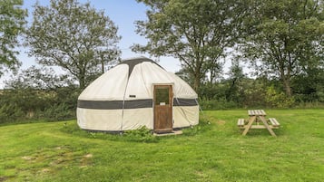 A dome-shaped tent with a door, set in a grassy area with trees in the background.