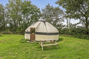 A single-room tent with a door and a small table in a grassy field. - Yurt Sleeps 2 - Bbq & Fire Pit - Dogs Welcome (Bodmin)