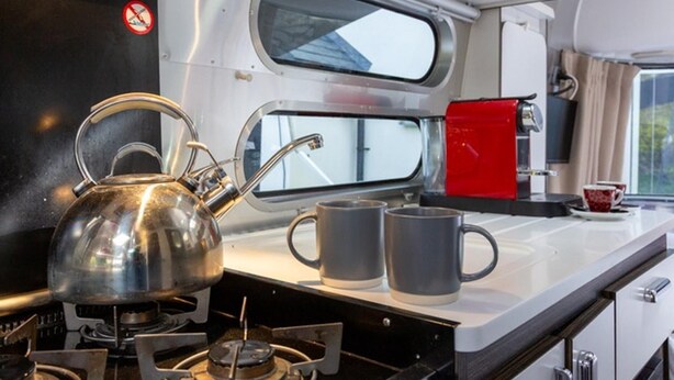 Une petite cuisine équipée d’une cuisinière à gaz, d’une bouilloire et de deux tasses posées sur le comptoir.