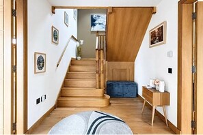Una escalera de madera con peldaños que conducen a una plataforma, un banco acolchado azul y una pequeña mesa de madera con un jarrón.