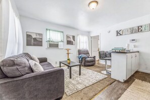 Una sala moderna con un sofá gris, una mesita y una zona de cocina con barra.