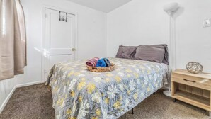 A bedroom with a bed, a bedside table, a lamp, and a door. - Coffield (Killeen)