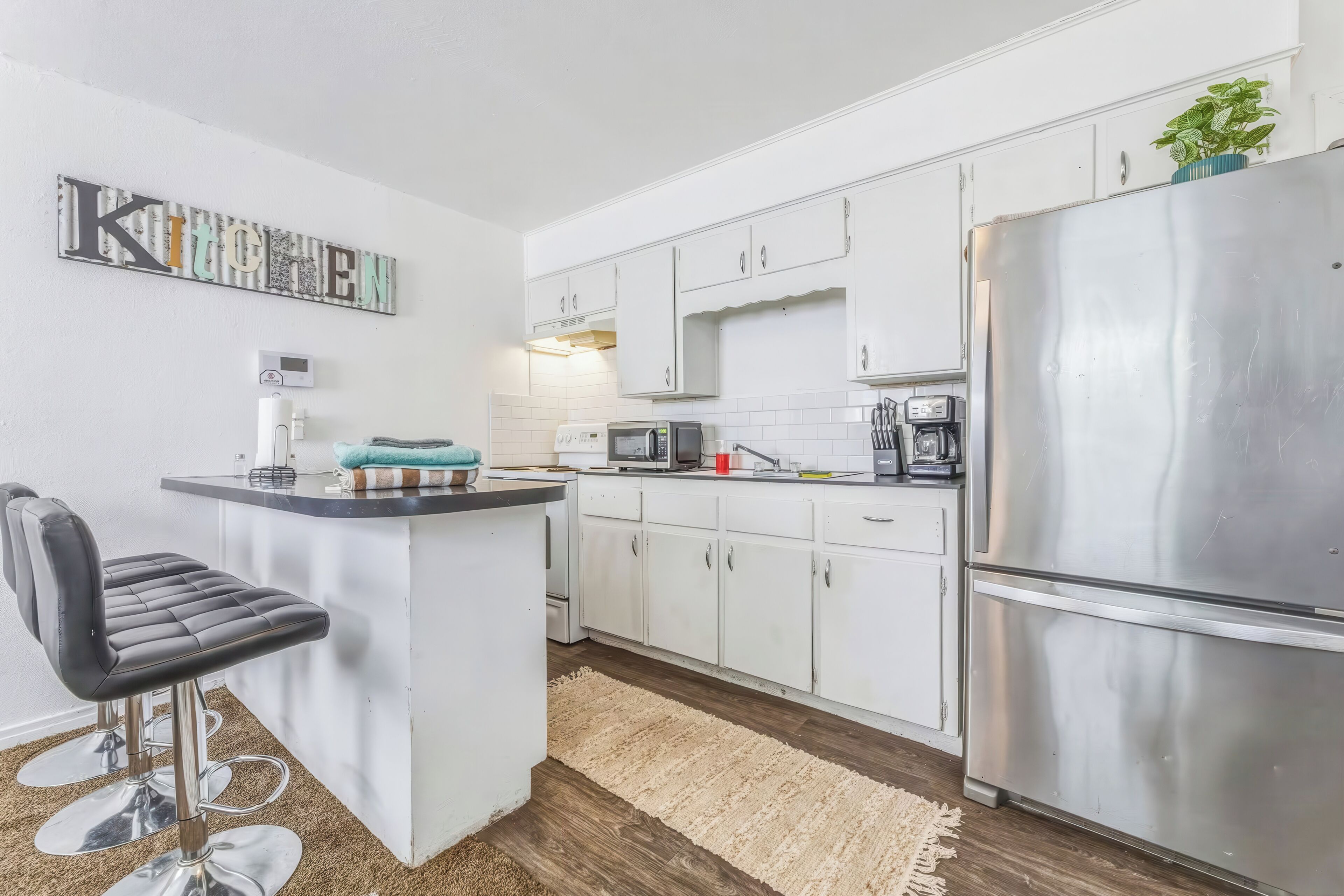 A modern kitchen with white cabinets, a stainless steel refrigerator, a microwave, and a coffee maker.
