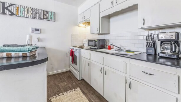A modern kitchen with white cabinets, a microwave, a coffee maker, and a stove. - Coffield (Killeen)