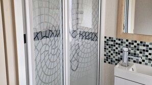 A bathroom with a glass-enclosed shower, a sink with a mirror, and a tiled backsplash. - Caravan Sleeps 6 With Parking (Great Yarmouth)