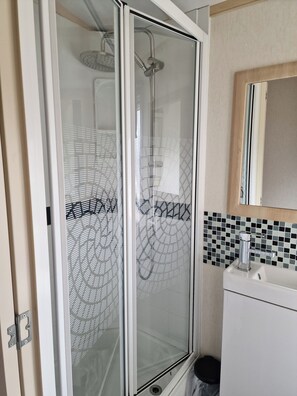 Ein Badezimmer mit einer Duschkabine, einem Waschbecken mit Spiegel und einer gefliesten Rückwand.