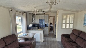 A modern kitchen with a central island, a dining area with a table and chairs, and a living area with sofas. - Caravan Sleeps 6 With Parking (Great Yarmouth)